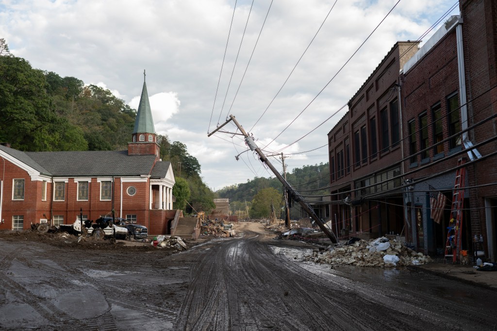 A damaged road with a church and a leaning power pole.
