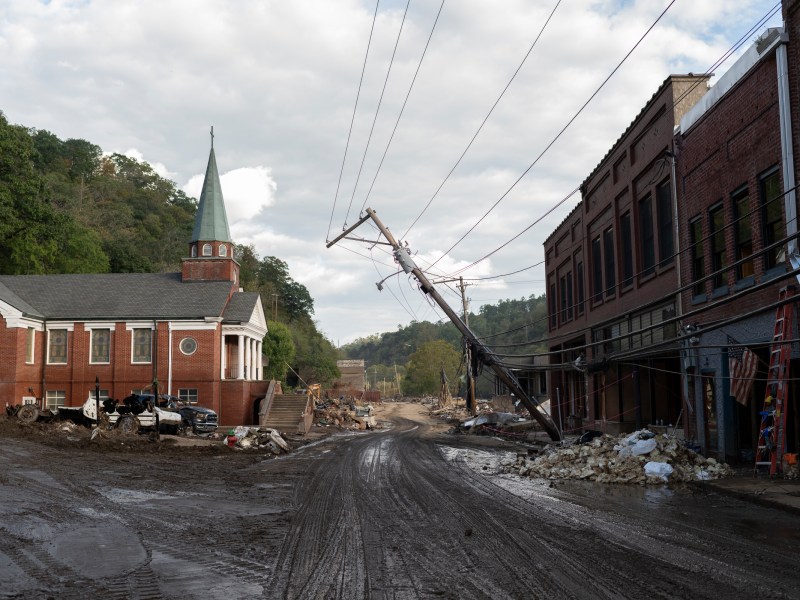 A damaged road with a church and a leaning power pole.