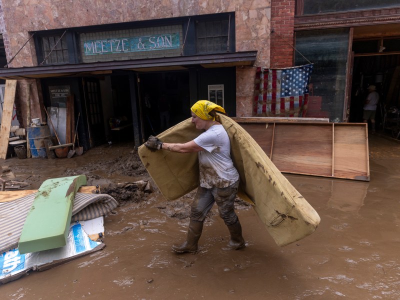 A woman carries a mattress through a muddy street as part of clean up after the French Broad River caused catastrophic flooding.