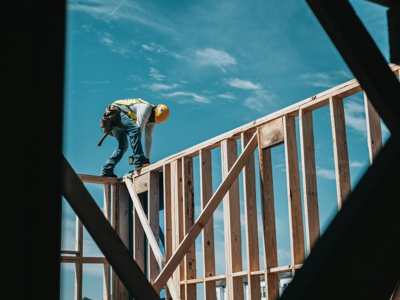 Man in a hardhat builds exterior frame of a house.