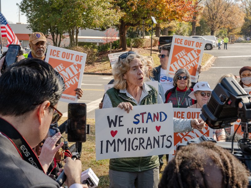 A crowd gathers around a woman holding a sign that reads We stand with immigrants.