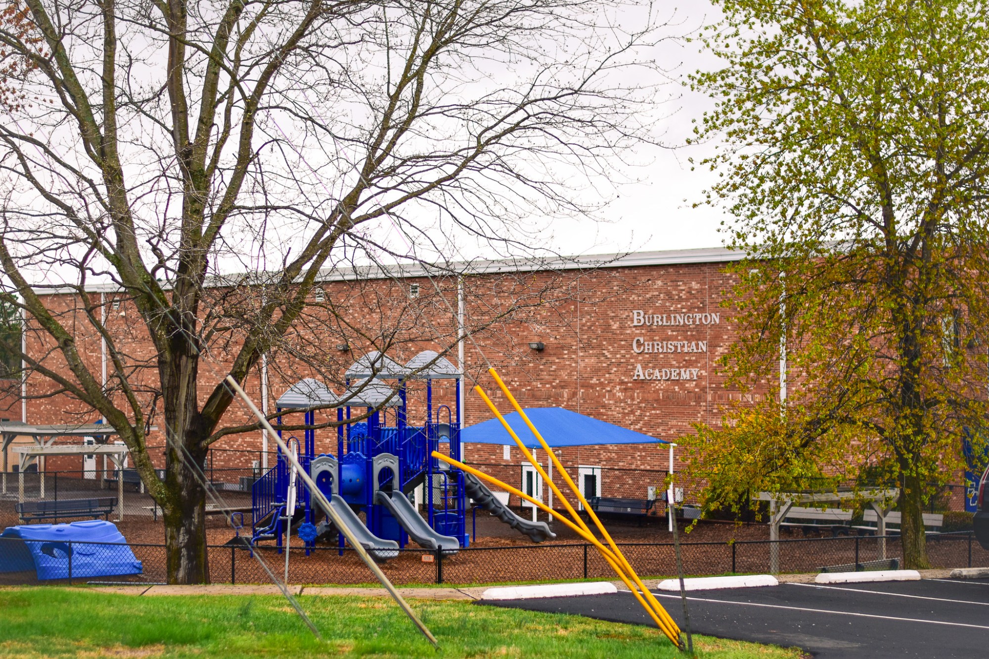 The brick exterior of Burlington Christian Academy with a blue playground and chain-link fence in the foreground.