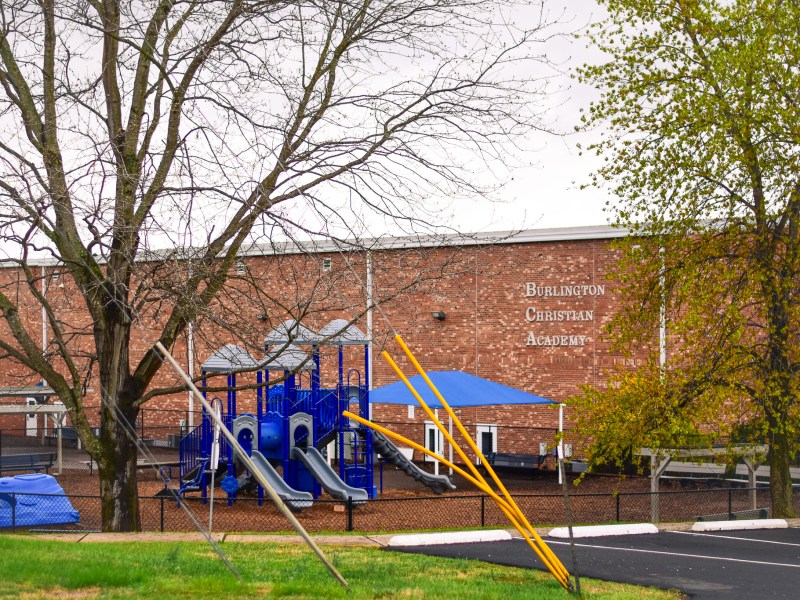 The brick exterior of Burlington Christian Academy with a blue playground and chain-link fence in the foreground.