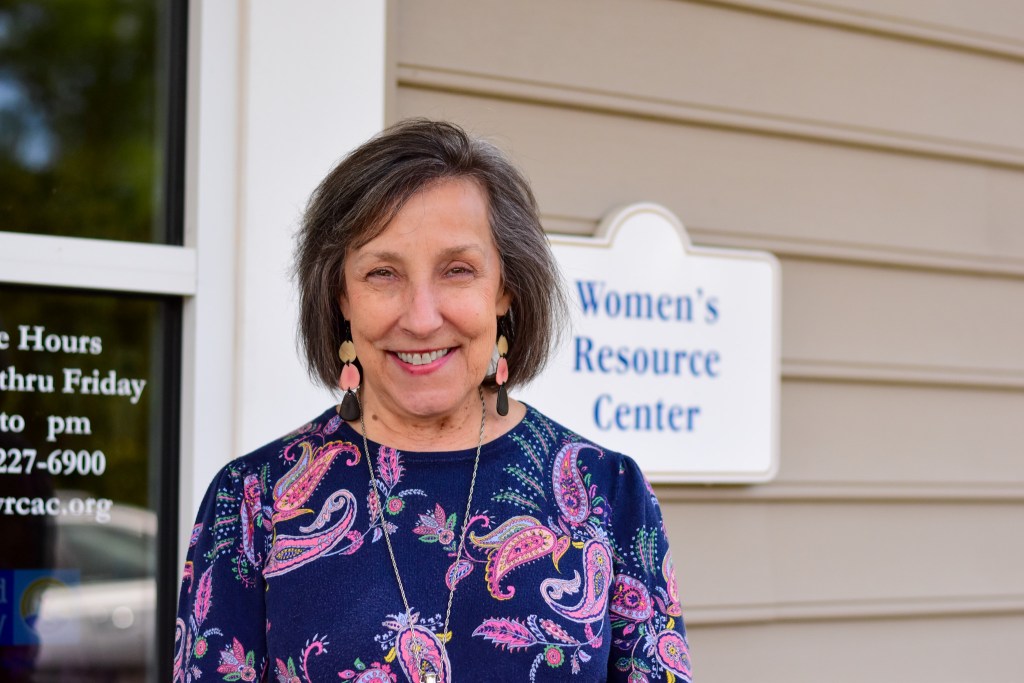 Susan Watson, Executive Director of the Women's Resource Center, smiling outdoors next to the center's sign.