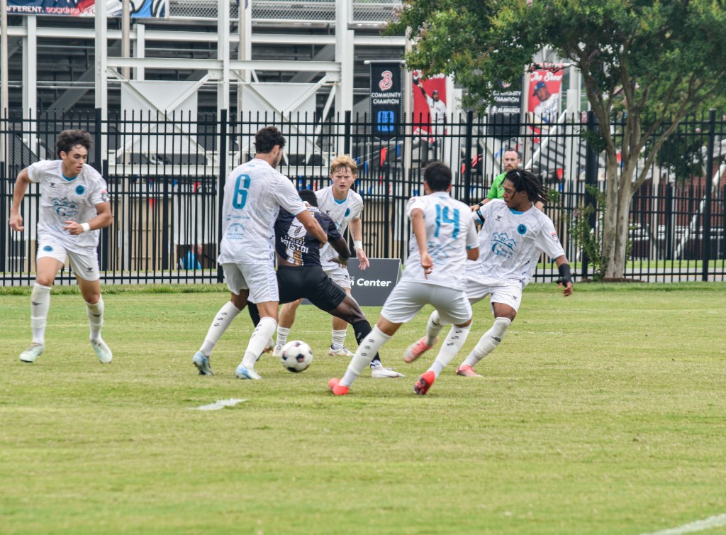 A group of Burlington United FC players surrounding a Bristol Rhythm AFC player to contest the ball.